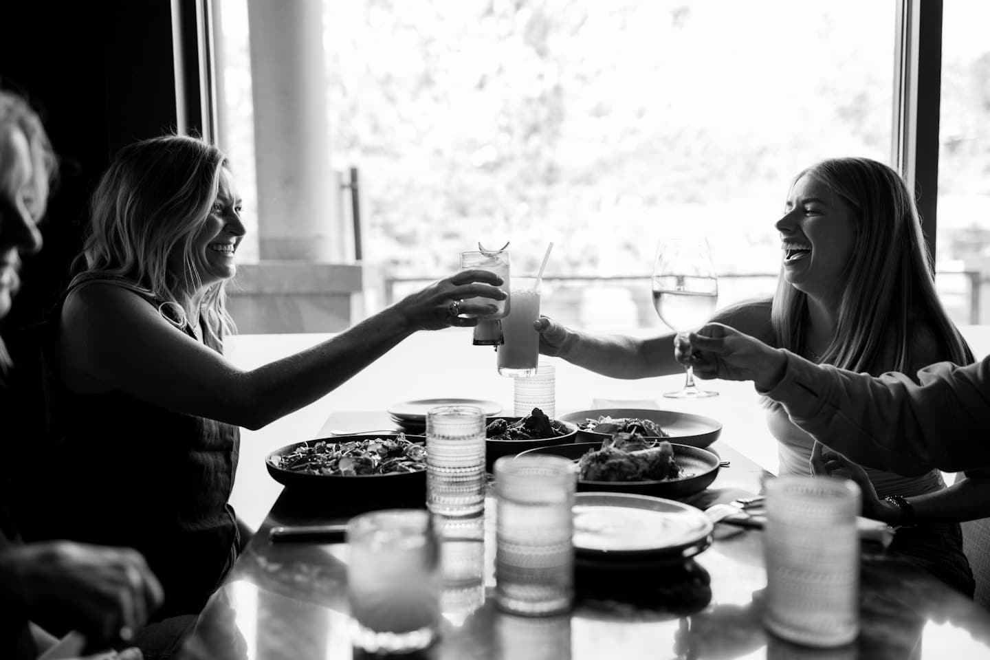 Due donne ridono e brindano con drink a un tavolo di ristorante.