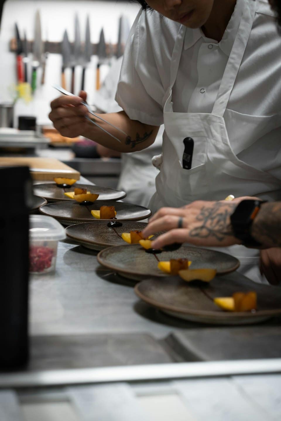 Chef che impiattano con precisione dessert elaborati in una cucina professionale.